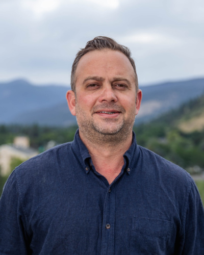 Headshot of Garrett Cathcart, a white man with a salt and pepper beard standing in front of scenic mountains