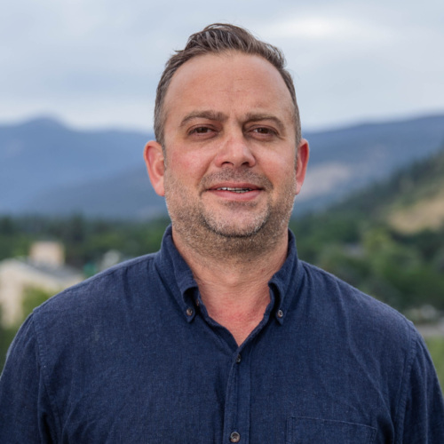 Headshot of Garrett Cathcart, a white man with a salt and pepper beard standing in front of scenic mountains