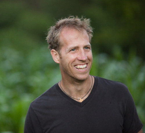 Jake Harriman, a tall white man with blonde hair, smiling in front of a grassy field