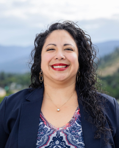 Headshot of Alice Garcia, a Latina woman with long curly black hair standing in front of scenic mountains