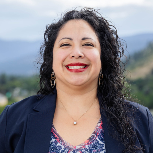 Headshot of Alice Garcia, a Latina woman with long curly black hair standing in front of scenic mountains