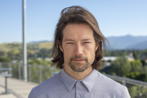 Headshot of Trip O'Connell, a Caucasian man with windswept light brown hair in a blue dress shirt with mountains in the background.